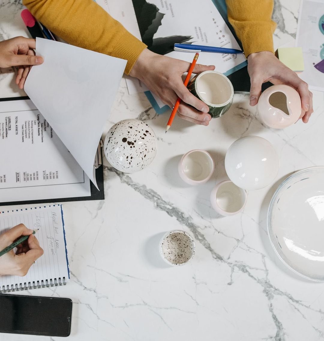 Overhead view of a product planning table with prototypes, costings and sketches