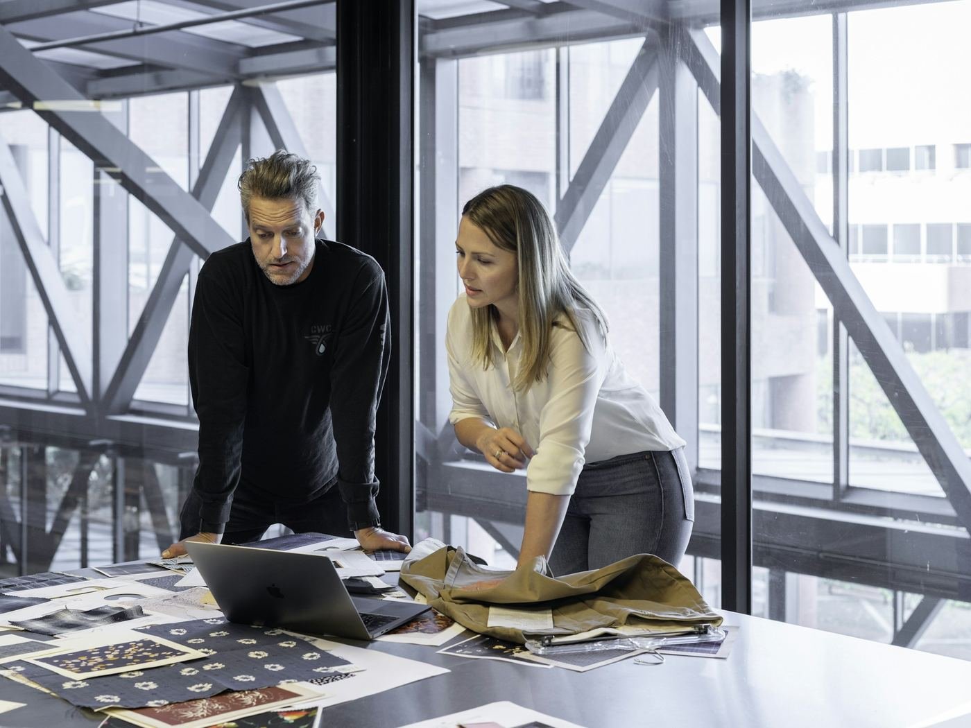 Two colleagues reviewing brand materials and product samples spread across a table in a bright, daylit studio